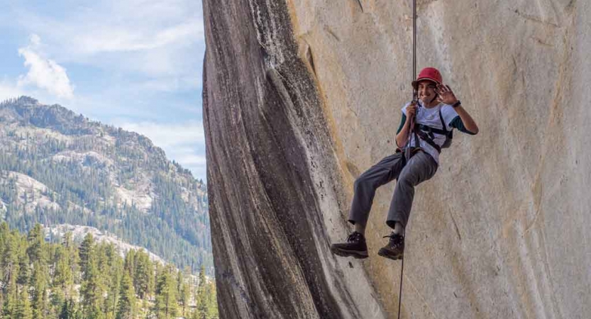 A student pauses to smile at the camera while rappelling down a rock wall 